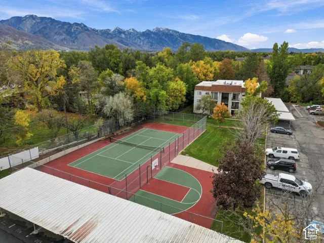 Recreational area featuring a tennis court, basketball hoop, and chain-link perimeter fencing, set against a mountain backdrop