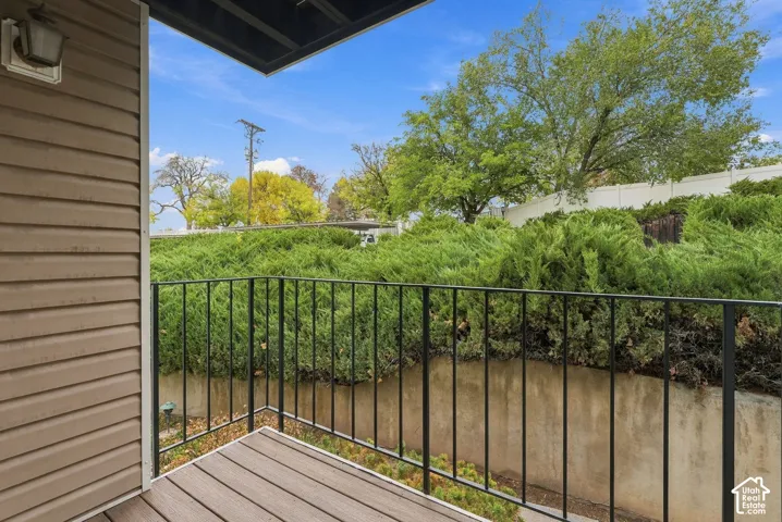 Private deck featuring composite wood-finish decking, black metal railings, and attached exterior lighting, complemented by a concrete retaining wall and mature landscaping