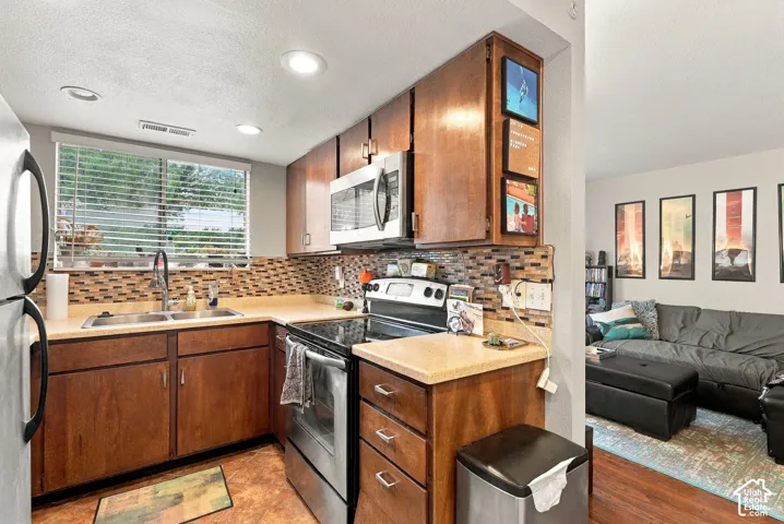 Kitchen featuring warm-toned cabinetry, stainless steel appliances, a multi-tone tile backsplash, recessed lighting, and solid-surface countertops