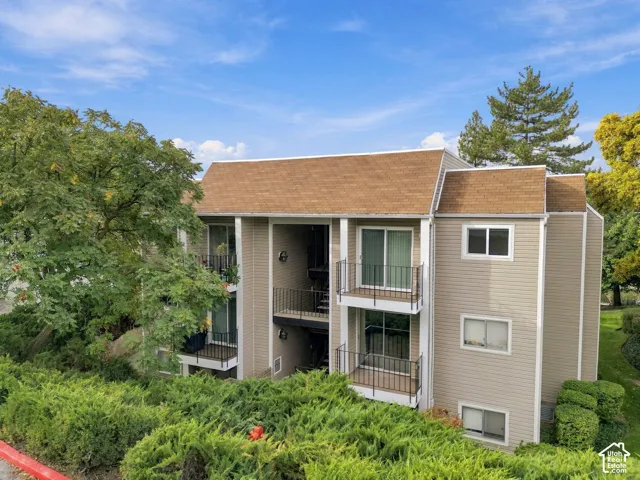 Multi-story building featuring horizontal siding, a pitched asphalt shingle roof, multiple private balconies with metal railings, and dual-pane sliding glass doors