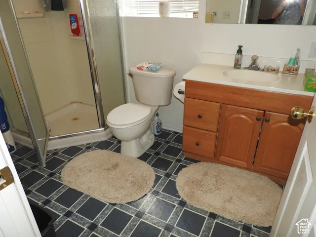 Bathroom featuring a corner glass-enclosed shower stall, wood-finish vanity with a white countertop and integrated sink, and patterned square-tile flooring