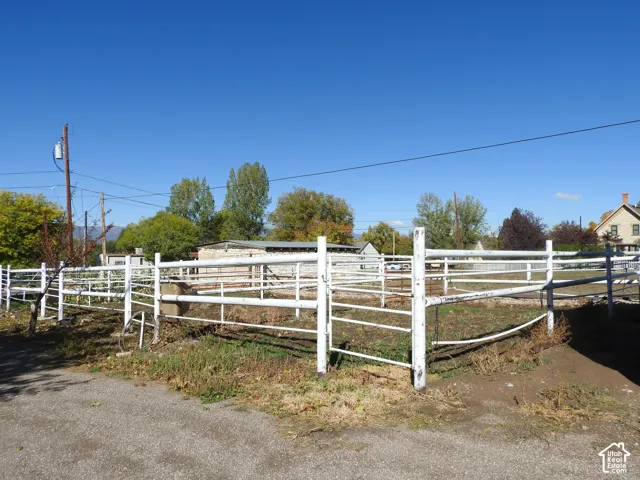 Fenced outdoor enclosure featuring white metal piping, open-air corrugated metal structure, and level earth terrain