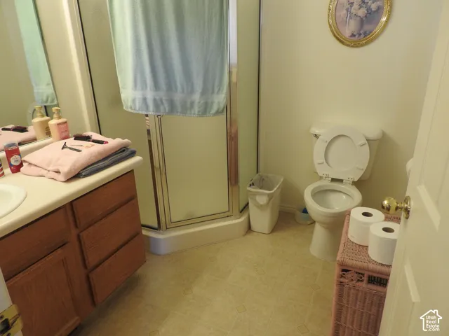 Bathroom featuring wood-finish cabinetry, integrated countertop with sink, corner shower enclosure with glass doors, and a standard toilet