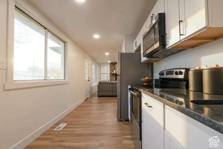 Kitchen featuring white shaker-style cabinetry, dark stone-finish countertops, stainless steel appliances, and wood-finish flooring