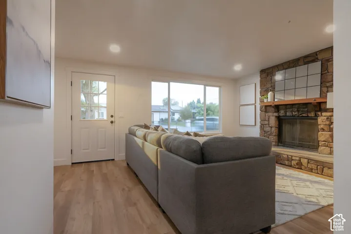 Living area featuring wood-finish flooring, a stone-surround fireplace, a horizontal wood mantel, recessed lighting, and a front entry door with a glass pane