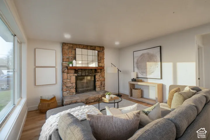 Living area featuring a floor-to-ceiling natural stone fireplace, raised stone hearth, wood mantel, and large picture window with wood-finish flooring