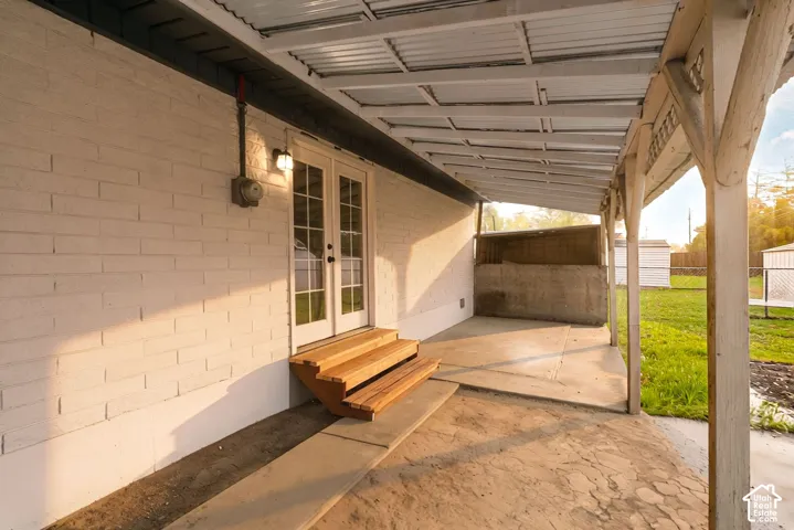 Covered exterior patio featuring a painted brick facade, French doors, wooden-finish steps, and a concrete slab