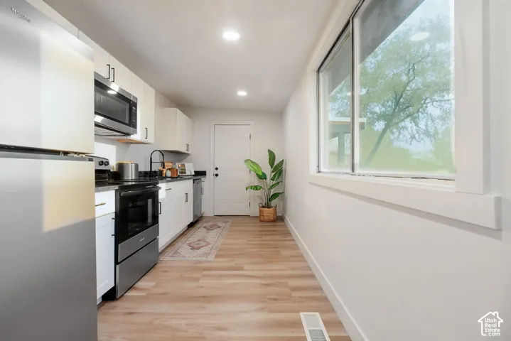 Kitchen featuring white cabinetry, dark countertops, stainless steel appliances, and wood-finish flooring