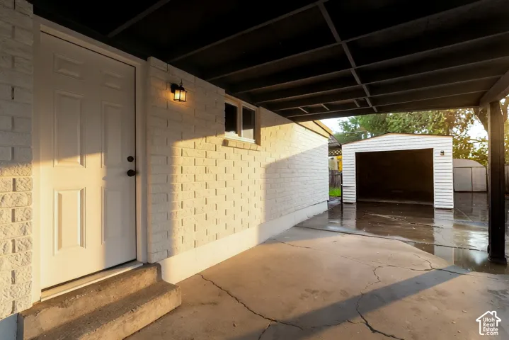 Covered carport featuring painted brick exterior walls, a concrete floor, an attached exterior light fixture, and a detached single-car garage