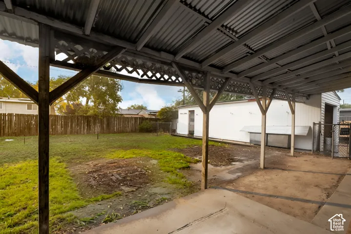 Covered patio featuring a corrugated metal roof, wood support beams, and decorative lattice trim, complemented by a fenced backyard