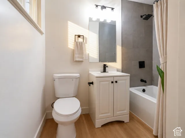 Bathroom featuring wood-finish flooring, a white vanity with a solid-surface countertop, matte black fixtures, a rectangular mirror, and gray tiled shower surround