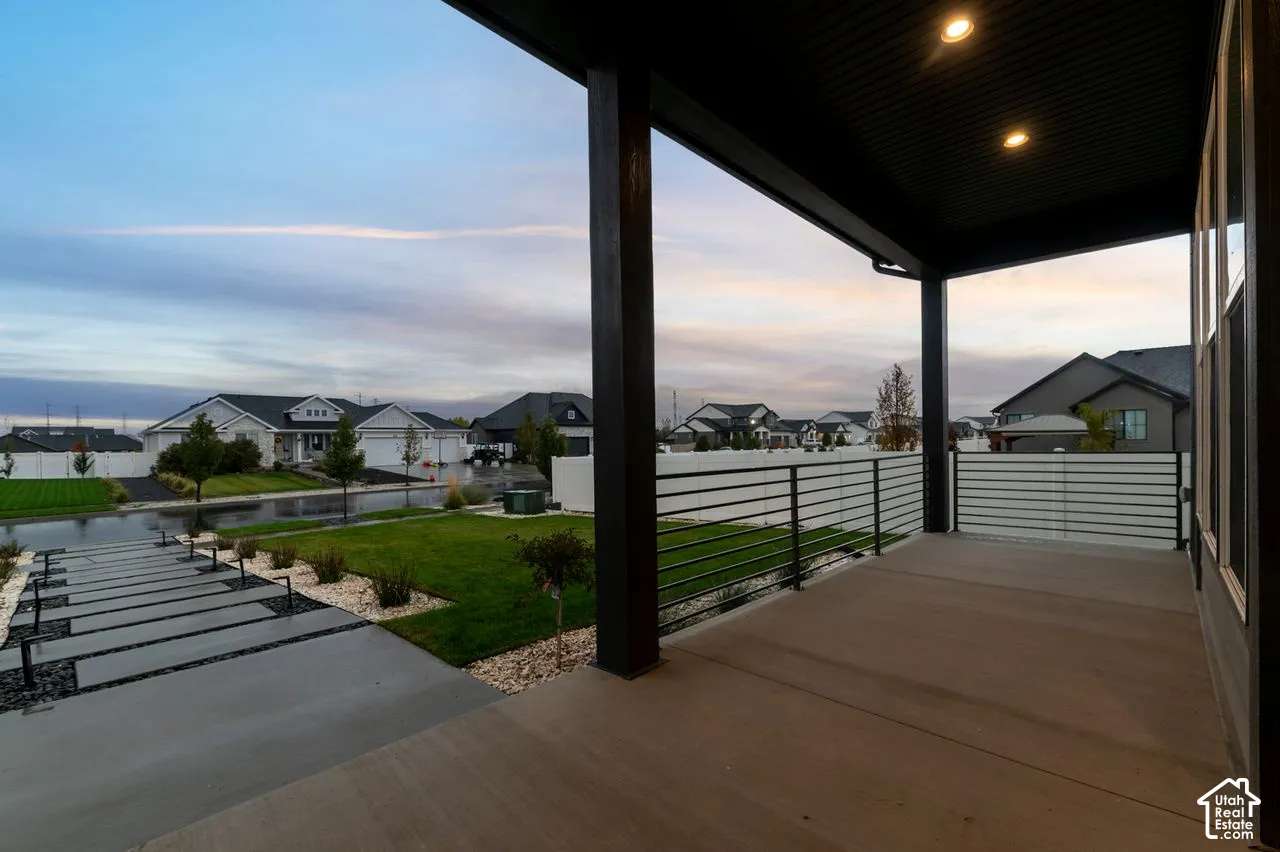 Covered patio featuring concrete flooring, a horizontal metal railing, and recessed ceiling lighting, complemented by a concrete paver walkway and landscaped lawn