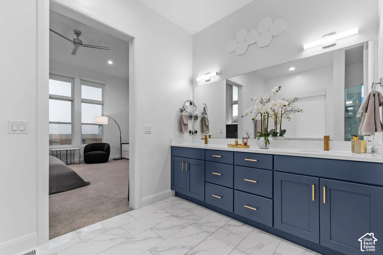 Dual-sink vanity with navy blue cabinetry, metallic hardware, and white stone-finish countertops, complemented by tile flooring, full-width vanity mirrors, and modern linear wall-mounted lighting