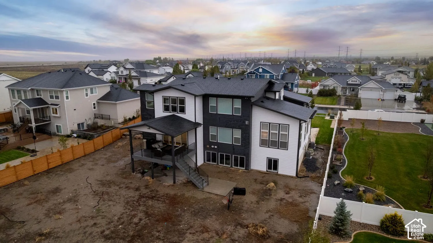 Two-story residence featuring a multi-tone exterior, dark shingle roof, covered elevated deck with railing, and large windows
