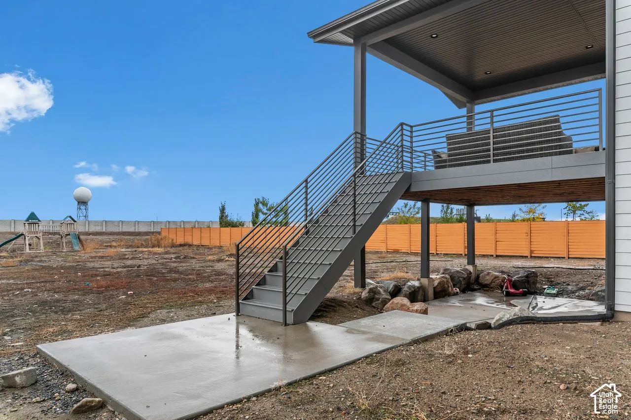 Covered deck featuring a metal horizontal-bar railing, integrated recessed lighting, concrete ground-level patio, and steel staircase with matching railing
