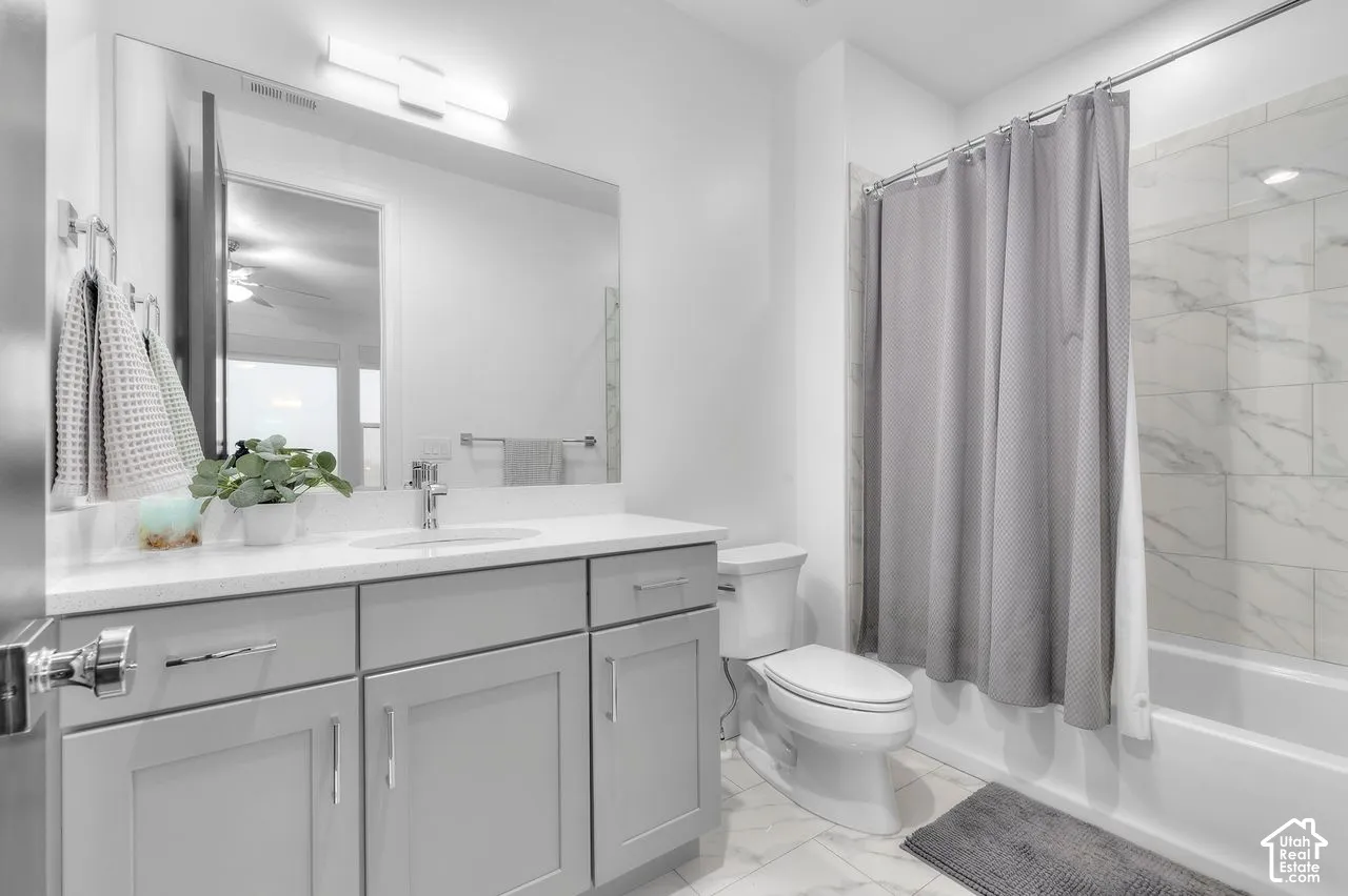 Bathroom featuring gray shaker-style cabinetry, white countertop with integrated sink, large wall-mounted mirror, and a tub-shower combination with full-height tile surround