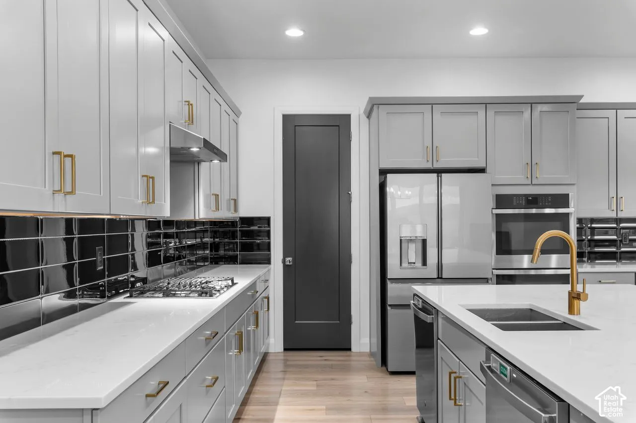 Kitchen featuring shaker-style cabinetry with gold-toned hardware, quartz countertops, black subway tile backsplash, built-in stainless steel appliances, and wood-finish flooring