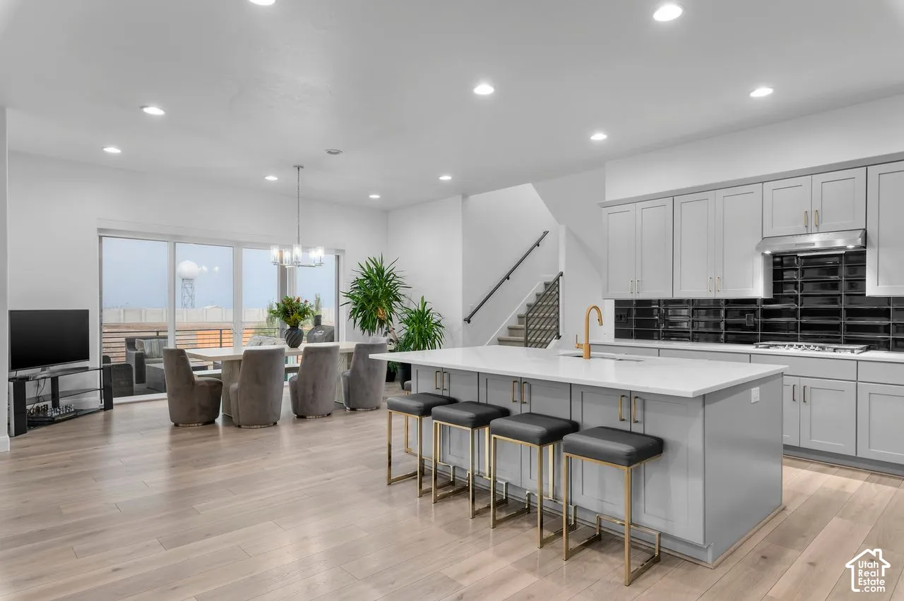 Open-concept kitchen featuring light-toned cabinetry, a spacious island with a neutral countertop, and a glossy black subway tile backsplash