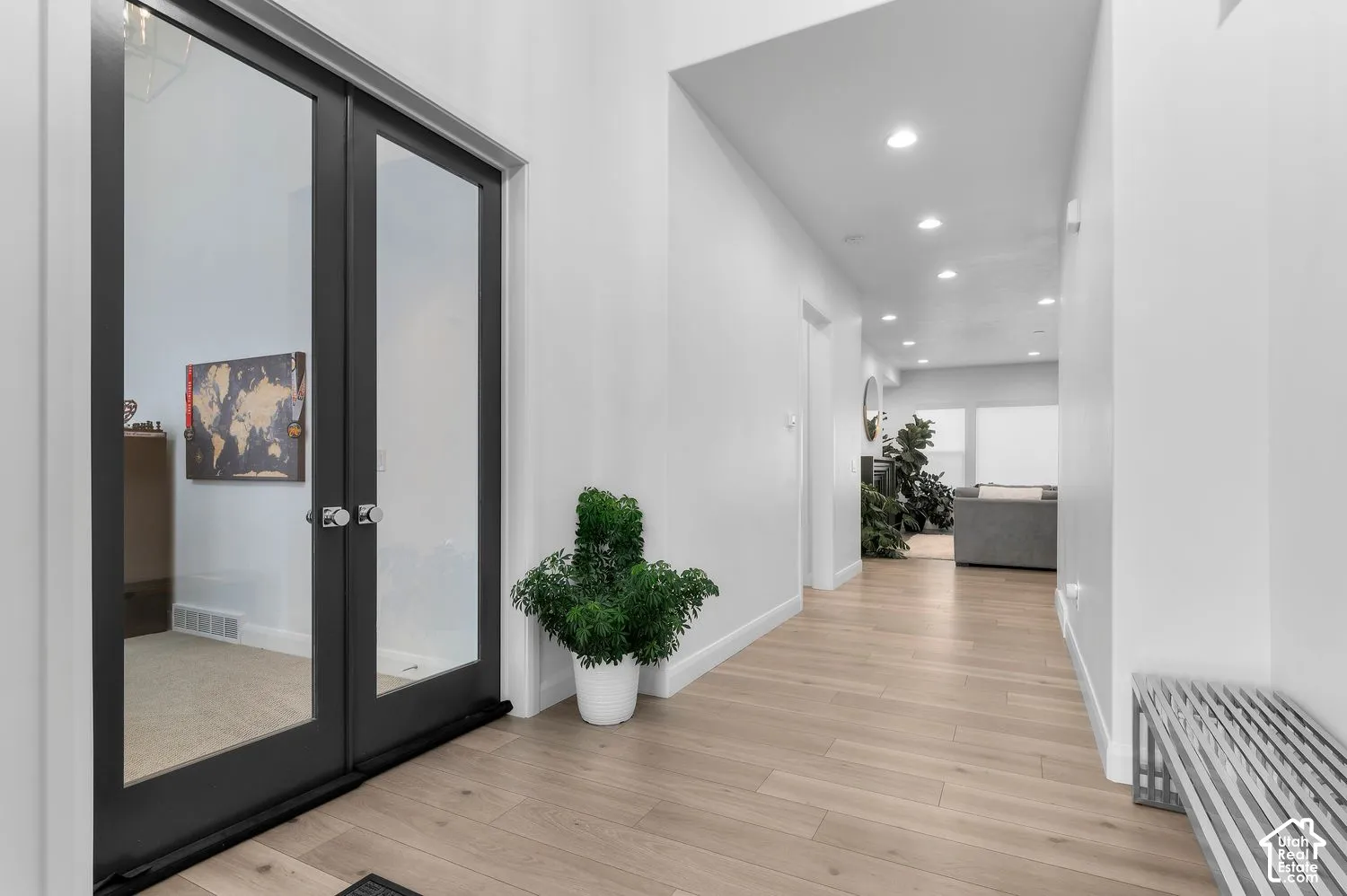 Hallway featuring light-toned wood-finish flooring, recessed ceiling lighting, and double doors with dark frames and glass panels