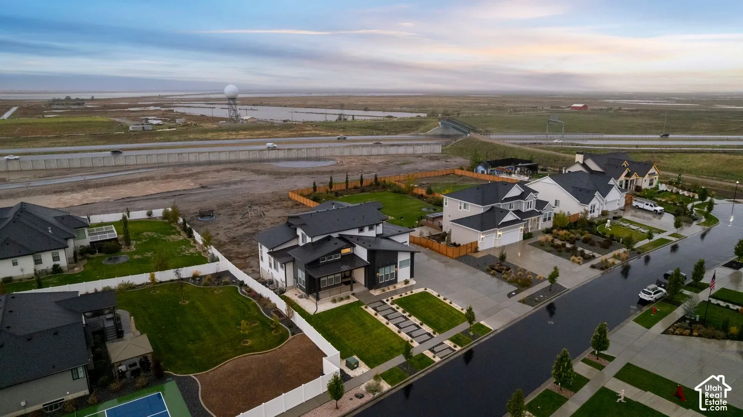 Aerial perspective of a multi-level residential structure featuring a dark metal roof, high-contrast exterior finishes, multi-car garage, and landscaped front yard with paved walkway