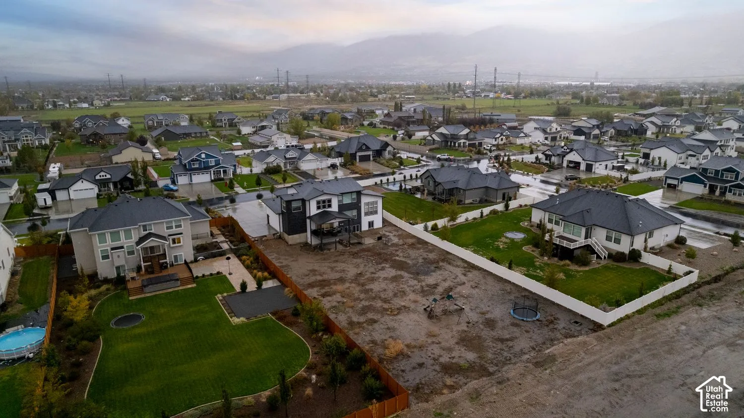 Aerial perspective of a residential neighborhood featuring multi-story dwellings, manicured lawns, varied fencing, and a prominent mountain backdrop