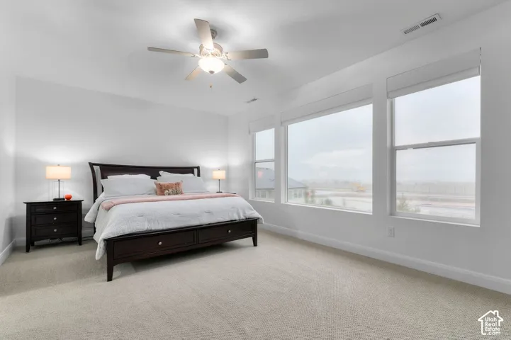 High-ceilinged room featuring carpeted flooring, a central ceiling fan with an integrated light fixture, and expansive windows
