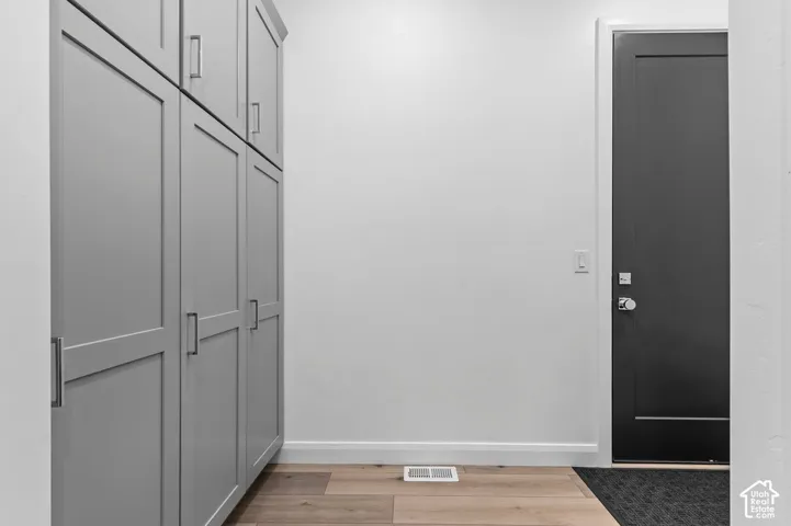 Grey floor-to-ceiling cabinetry featuring shaker-style doors and silver hardware, complemented by wood-finish flooring and a charcoal-finished door