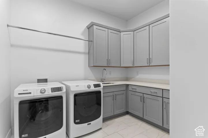 Laundry area featuring grey shaker-style cabinetry, solid-surface countertops, an undermount sink with a gooseneck faucet, tile flooring, and a wall-mounted metal hanging rod