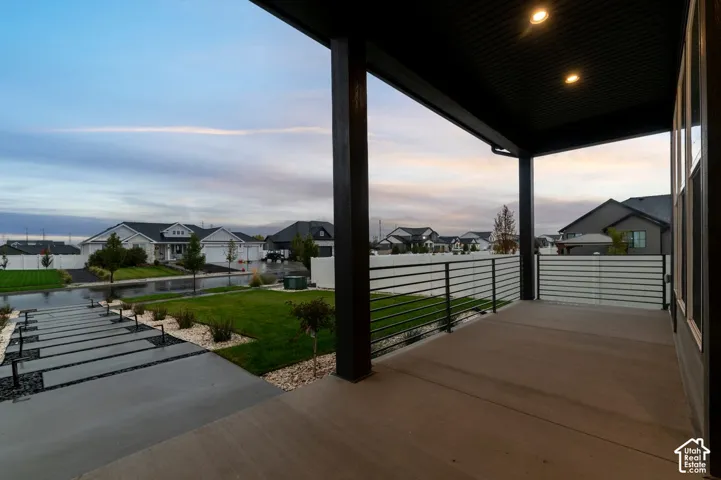 Covered patio featuring concrete flooring, a horizontal metal railing, and recessed ceiling lighting, complemented by a concrete paver walkway and landscaped lawn