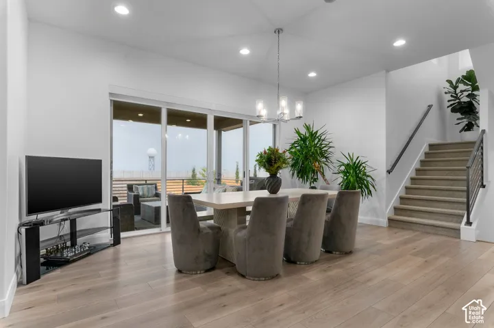 Open-concept room featuring wide-plank wood-finish flooring, recessed lighting, a modern multi-light chandelier, sliding glass doors to an exterior space, and a carpeted staircase with a metal handrail