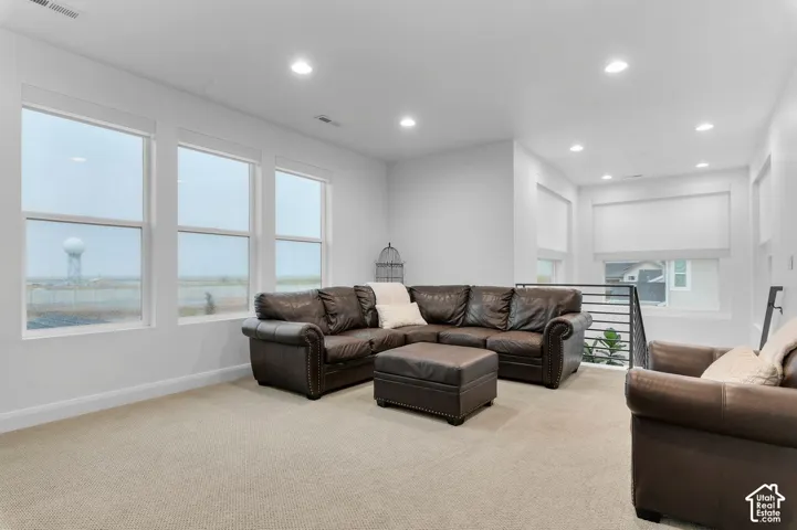 Living area featuring large windows, recessed lighting, neutral carpeting, and a horizontal bar metal railing