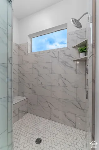 Walk-in shower featuring large-format rectified tile walls, hexagonal mosaic floor tile, a built-in tiled bench, polished chrome shower head, and a transom window