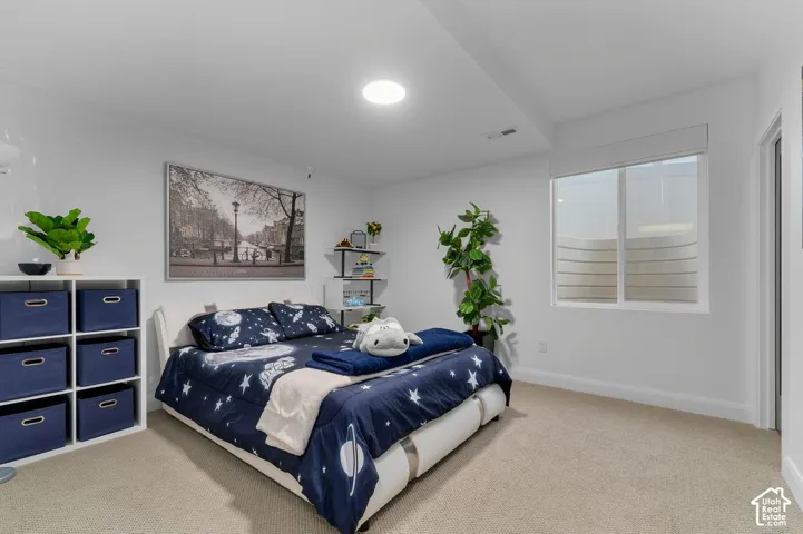 Neutral-toned interior space featuring light-colored wall-to-wall carpeting, recessed ceiling lighting, and a window with a structured window well