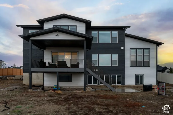 Two-story exterior featuring dual-tone siding, a covered deck with horizontal metal railings, multiple large windows, and a concrete patio