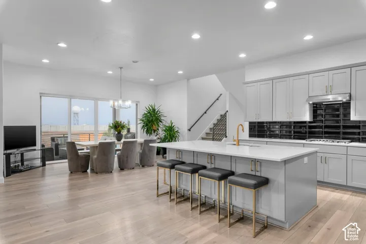 Open-concept kitchen featuring light-toned cabinetry, a spacious island with a neutral countertop, and a glossy black subway tile backsplash