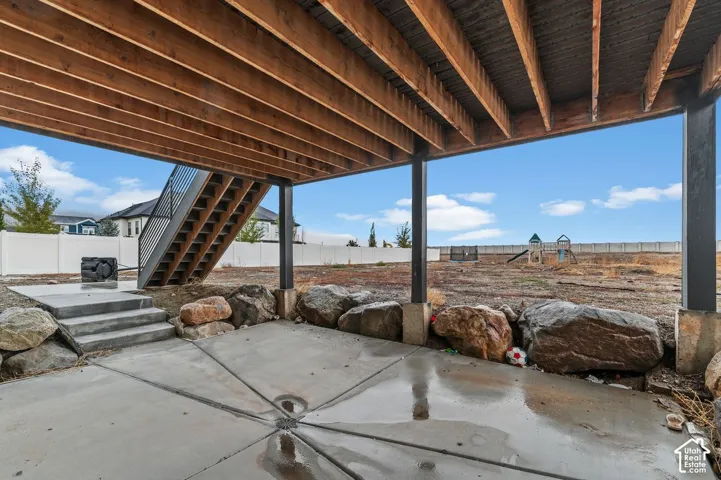 Covered concrete patio featuring exposed wooden support beams, natural boulder retaining elements, and metal exterior staircase