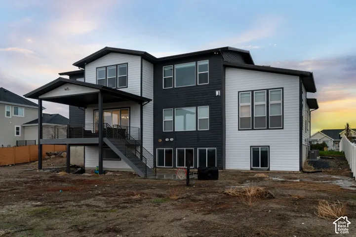 Two-story exterior featuring high-contrast horizontal siding, a covered rear deck, metal railings, and a staircase leading to the lower level