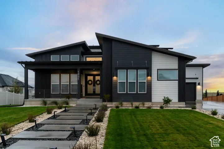 Modern exterior featuring contrasting dark and white horizontal siding, asymmetrical shed roof lines, a concrete paver walkway with integrated landscape lighting, and a covered front porch with metal railing