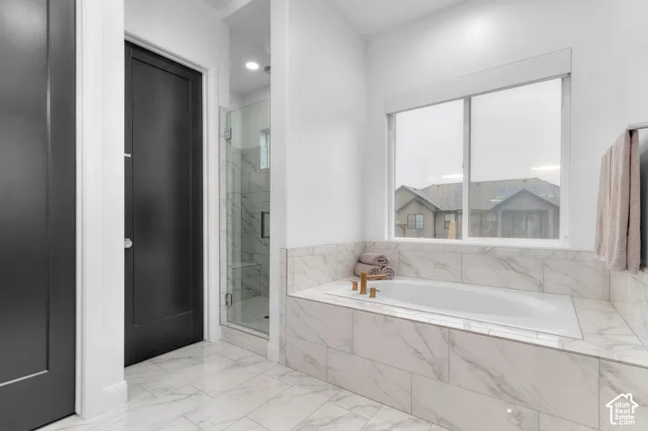 Deep soaking tub with a tiled surround, glass-enclosed walk-in shower with stone-patterned tile, matte black door hardware, and oversized tile flooring