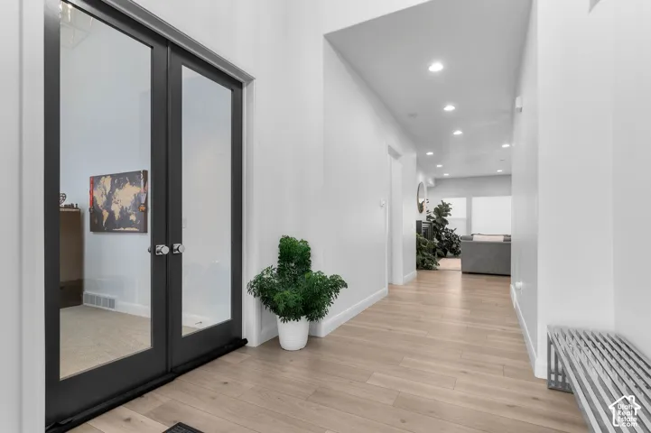 Hallway featuring light-toned wood-finish flooring, recessed ceiling lighting, and double doors with dark frames and glass panels