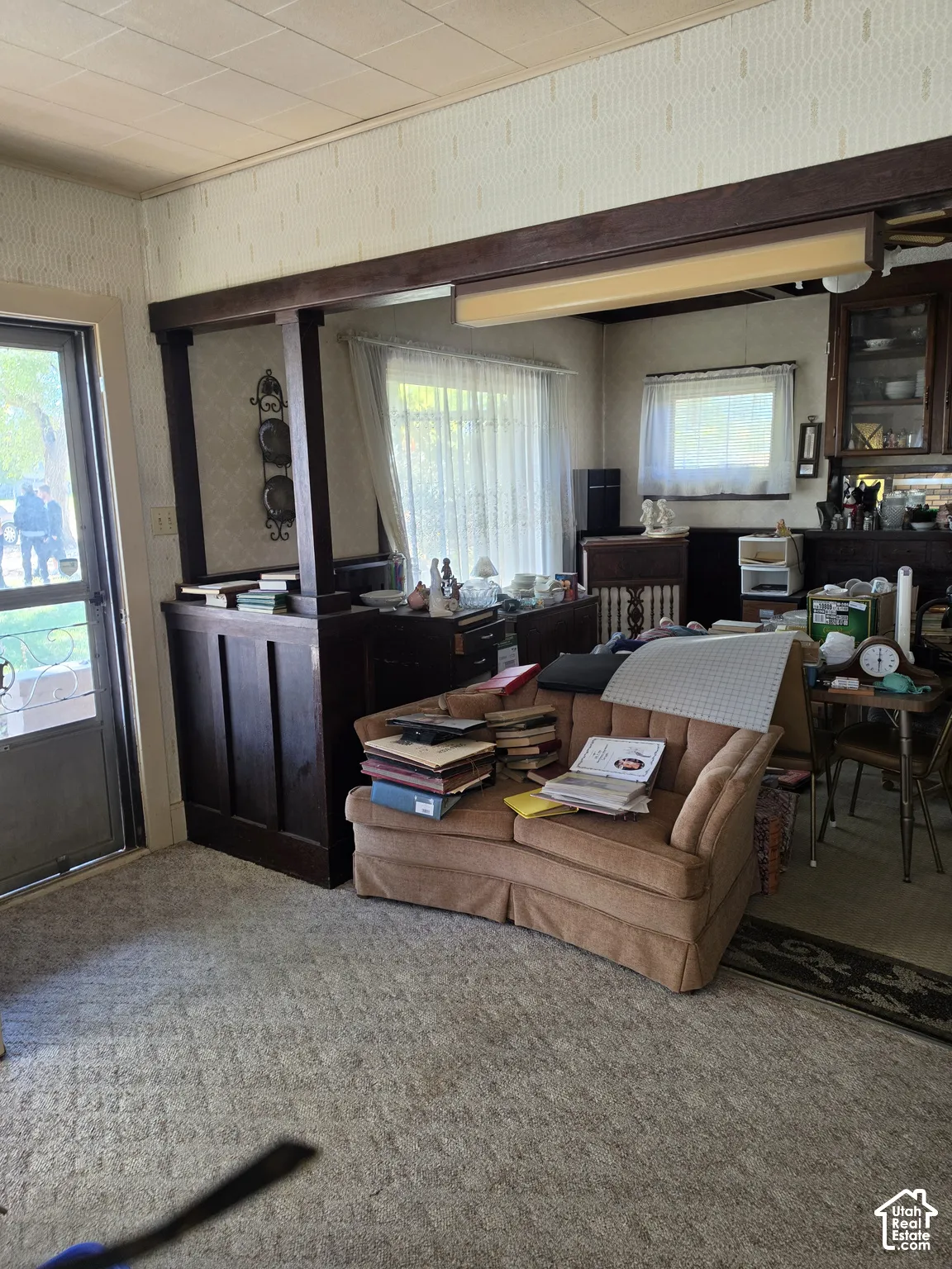 Interior featuring dark-stained wood half-wall partition with structural post, built-in glass-front cabinetry, and window with textile valance