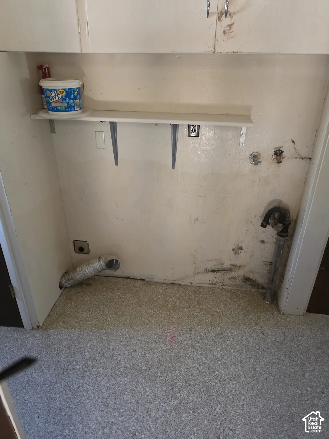 Utility area featuring wall-mounted upper cabinetry, a fixed shelving unit, dedicated plumbing hookups, and integrated ventilation ducting