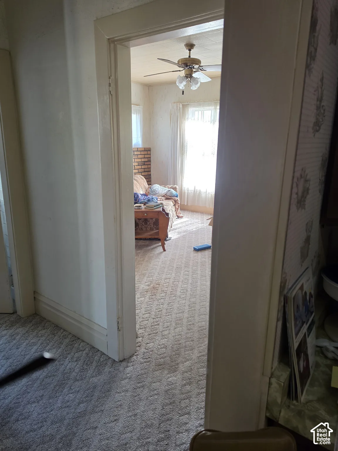 Interior doorway featuring structured wooden casing, ceiling fan with light fixture, brick masonry accent wall, and patterned wallcovering
