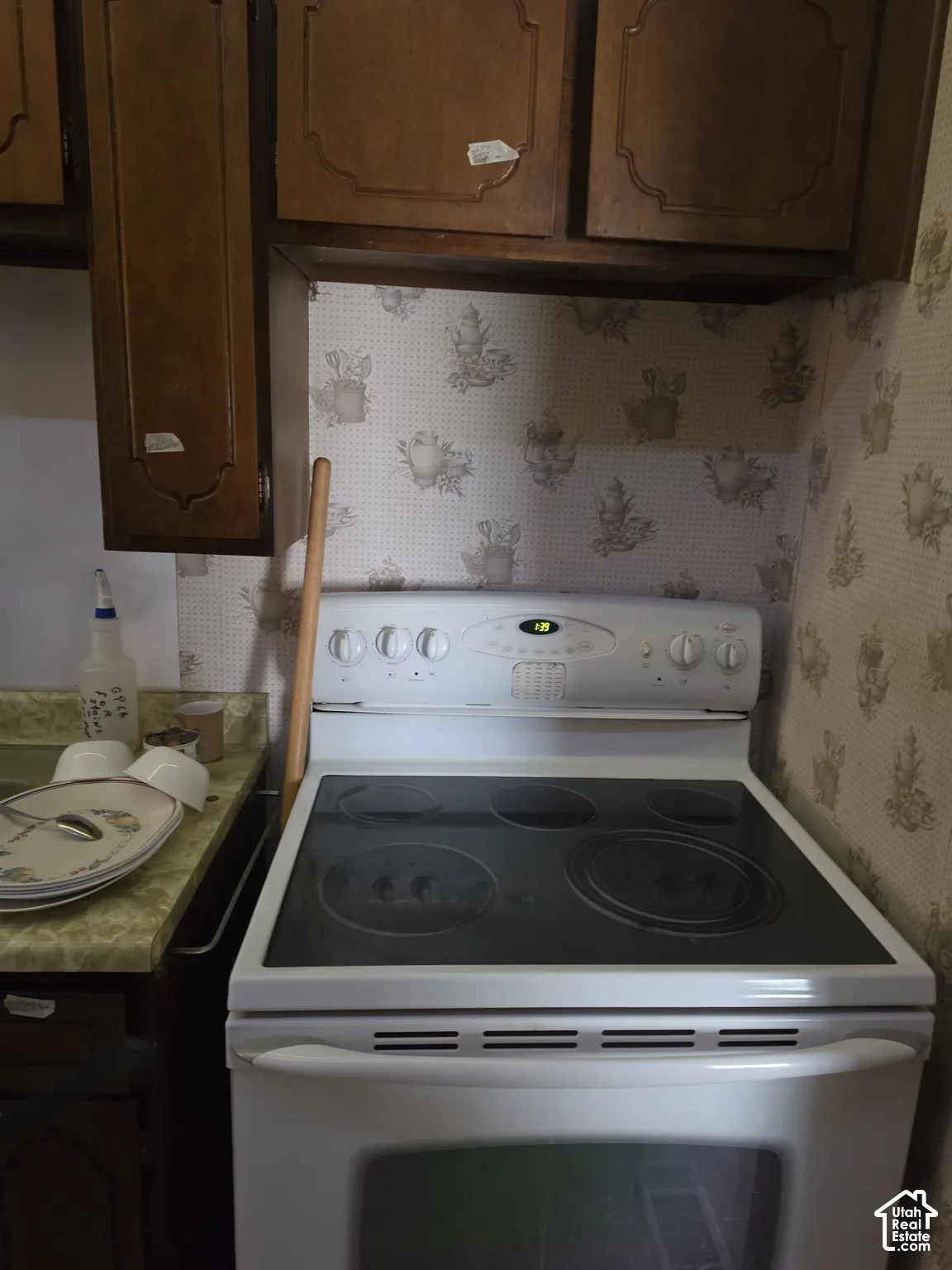 Wall-mounted wood cabinetry, patterned wall covering, and a white freestanding electric range with a glass cooktop