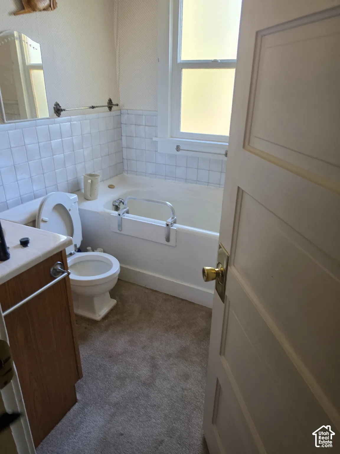 Bathroom featuring a wood-finish vanity with a solid-surface countertop, tile tub surround, and a single-hung window with a classic multi-panel door