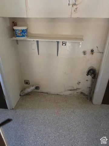 Utility area featuring wall-mounted upper cabinetry, a fixed shelving unit, dedicated plumbing hookups, and integrated ventilation ducting