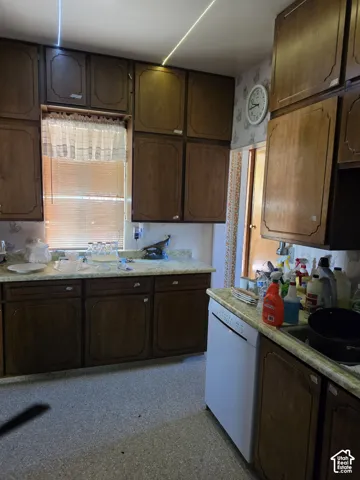 Kitchen featuring wood cabinetry with raised-panel detailing, light-toned laminate countertops, and a white built-in dishwasher