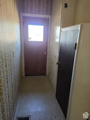 Built-in floor-to-ceiling storage cabinetry with white doors, additional dark-finish cabinet, exterior door with integrated window, and patterned wall covering