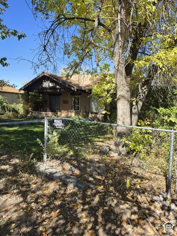 Single-story residence featuring a covered front porch, stone-accented pillars, and mature trees on the grounds
