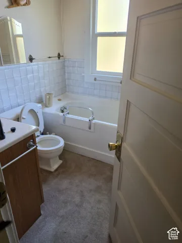 Bathroom featuring a wood-finish vanity with a solid-surface countertop, tile tub surround, and a single-hung window with a classic multi-panel door